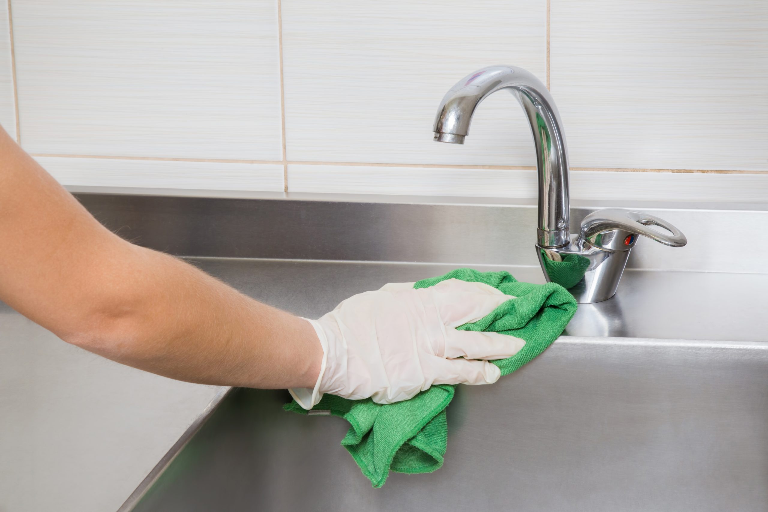 Hand in protective glove with rag cleaning commercial kitchen sink